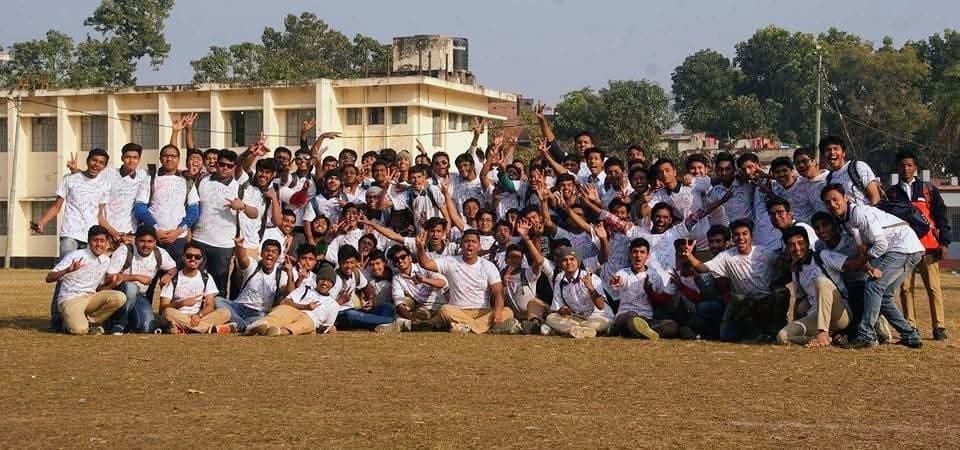The whole batch on the school field in signed white shirts, the building behind them.