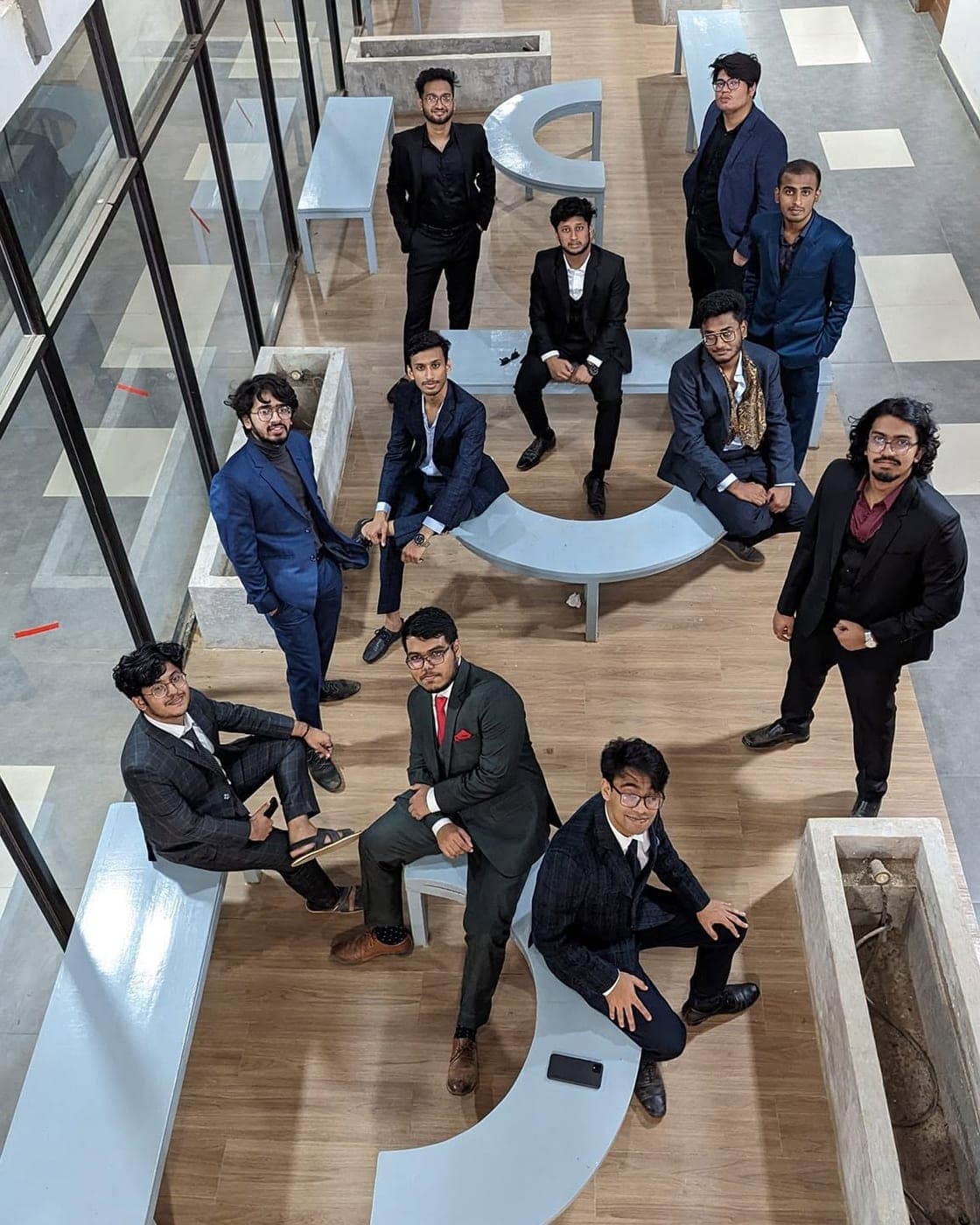 Twelve of us in suits in a campus atrium, photographed from the floor above.